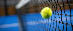 Ein gelber Ball fällt in ein schwarze Netz, das auf einem blauen Padel Court steht