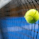 Ein gelber Ball fällt in ein schwarze Netz, das auf einem blauen Padel Court steht